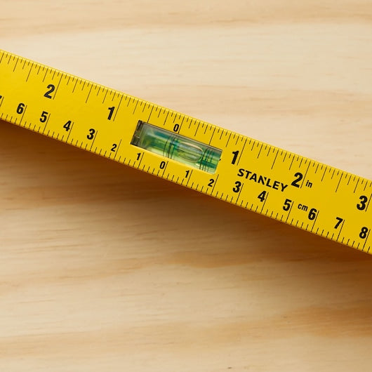 A close-up of the STANLEY 42-328 Heavy Duty Aluminum I-Beam Level with a rotating vial for precision leveling on a wooden surface, featuring both inches and centimeters.