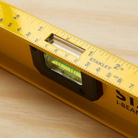 A close-up of the STANLEY 42-328 48 in. Heavy Duty Aluminum I-Beam Level with a 180° rotating vial, placed on wood. It features a bubble vial for angles, with a ruler in inches and centimeters along its edge.