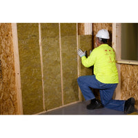 In a partially built structure, a worker wearing a bright yellow shirt and hard hat kneels to install Go Builds R15 Thermafiber Fire and Sound Guard 15 in. x 47 in. Mineral Wool Insulation Batt between wooden studs for improved fire and sound protection.