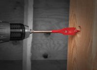 A DIABLO DSP1010 3/8 in. x 4 in. Spade Bit for Wood by Diablo is horizontally drilling a hole into a light-colored wooden board with visible grain patterns, while blurred structural beams can be seen faintly in the background.