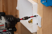 Close-up of someone using a Diablo DIABLO DPH235P1 Phillips drive bit power drill on wood, with black gloves. The drill has an Impact Strong™ red extension bit. A white bracket and part of a blue object are visible in the background.