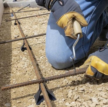 A person wearing gloves uses the GRIP-RITE BTTWEAR Bar Tie Wire Twister tool by Grip-Rite to secure metal bars on a construction site. Various tools and accessories, like rollers and hand tools, are displayed below alongside product descriptions emphasizing Secure Connections for home.